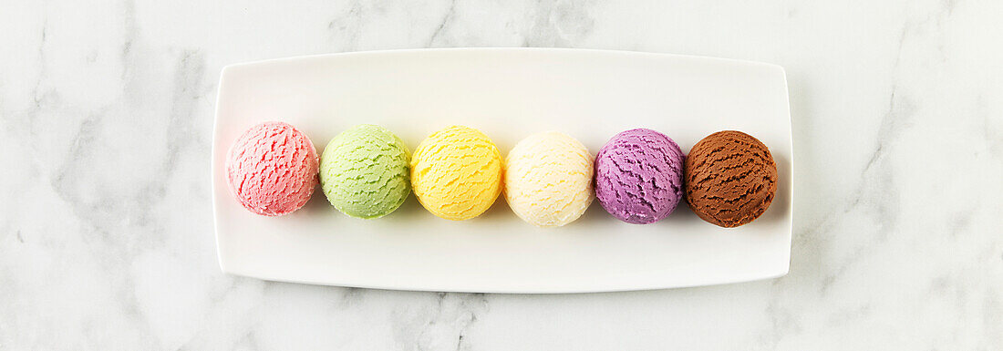 Set of various ice cream scoops on white marble background. Strawberry, pistachio, mango, vanilla, blueberry and chocolate ice cream. Top view, flat lay
