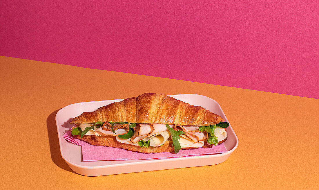 Leckeres Croissant mit Schinken, Käse und Rucola auf einem Teller mit buntem Hintergrund von oben