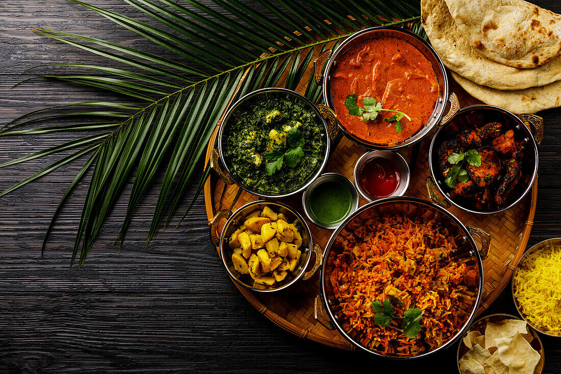 Indisches Essen Curry-Butterhähnchen, Palak Paneer, Chiken Tikka, Biryani, Gemüsecurry, Papad, Dal, Palak Sabji, Jira Alu, Reis mit Safran auf dunklem Hintergrund