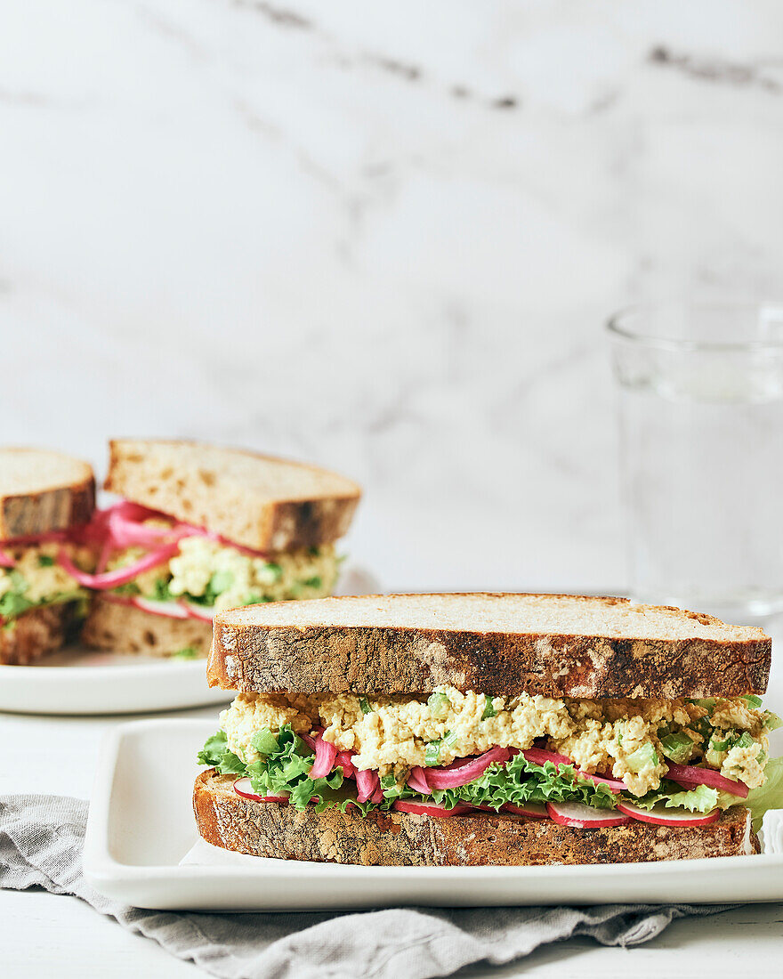 Tofu-Salat-Sandwich auf weißem Tablett mit grauer Serviette