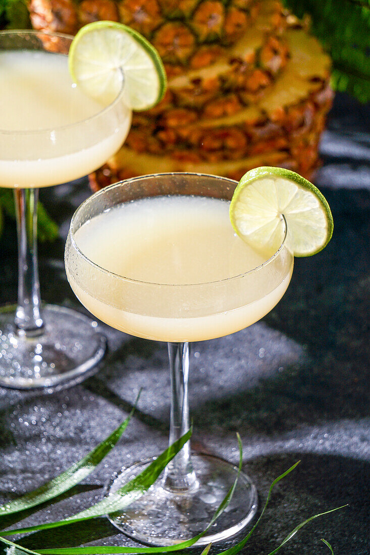 Sommercocktail Ananas-Daiquiri mit Wodka, Ananassaft, gefrorener Bewegung und fliegenden Tropfen. Tropischer Hintergrund mit Palmenblättern