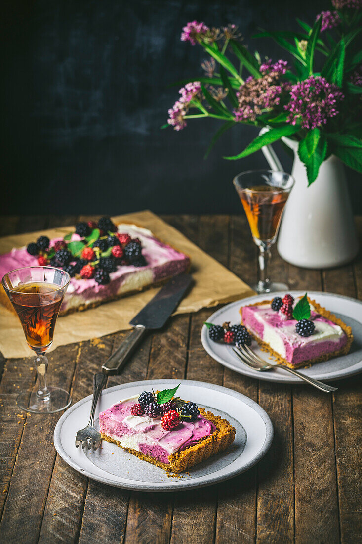 Cheesecake and berries on parchment with slices on serving plates and glasses with sherry