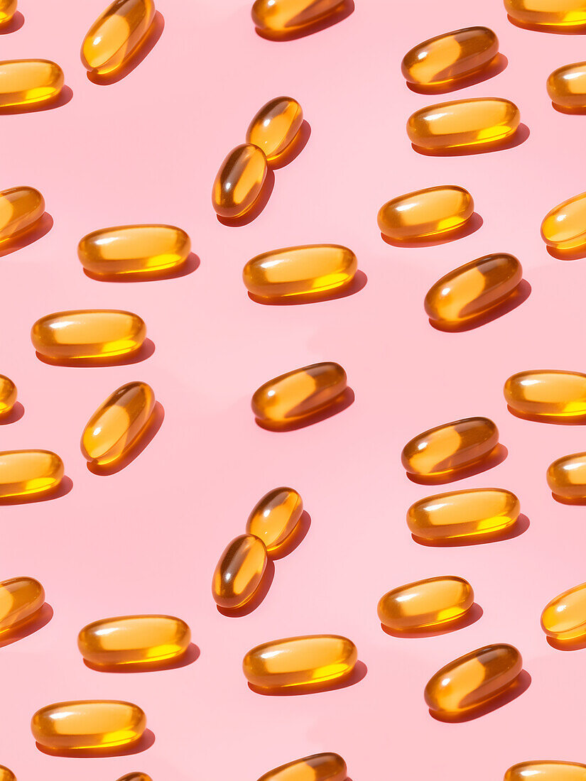Composition of orange vitamin pills on a pink background in a bright studio viewed from above