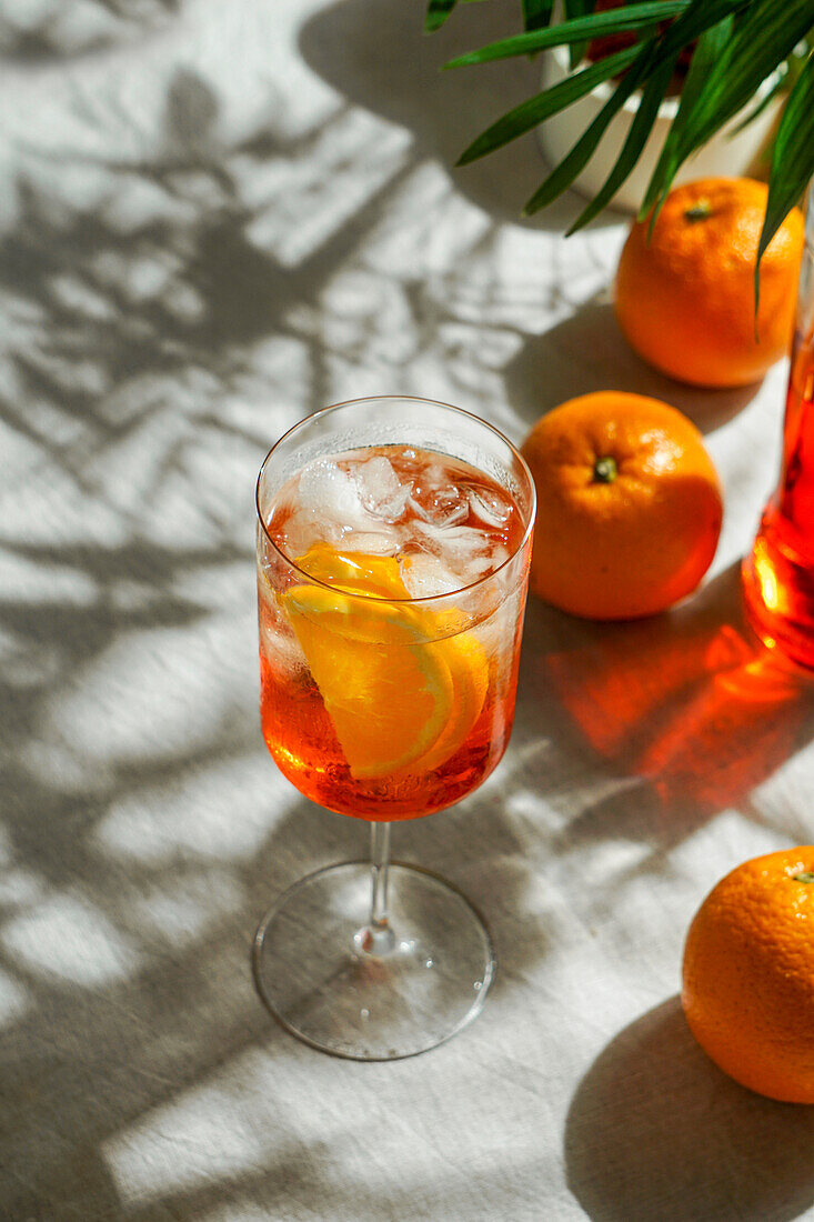 Aperol Spritz, Cocktail, auf einer Leinentischdecke, Schatten, hartes Sonnenlicht, Sommergetränk im Glas