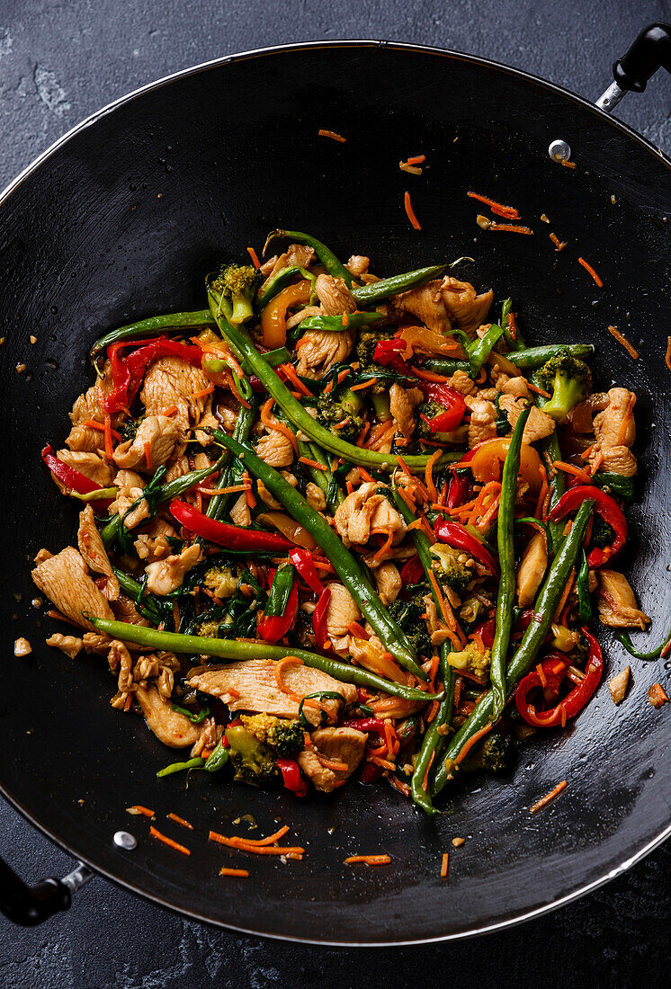 Stir-fried chicken with peppers and green beans in a wok pan, close-up