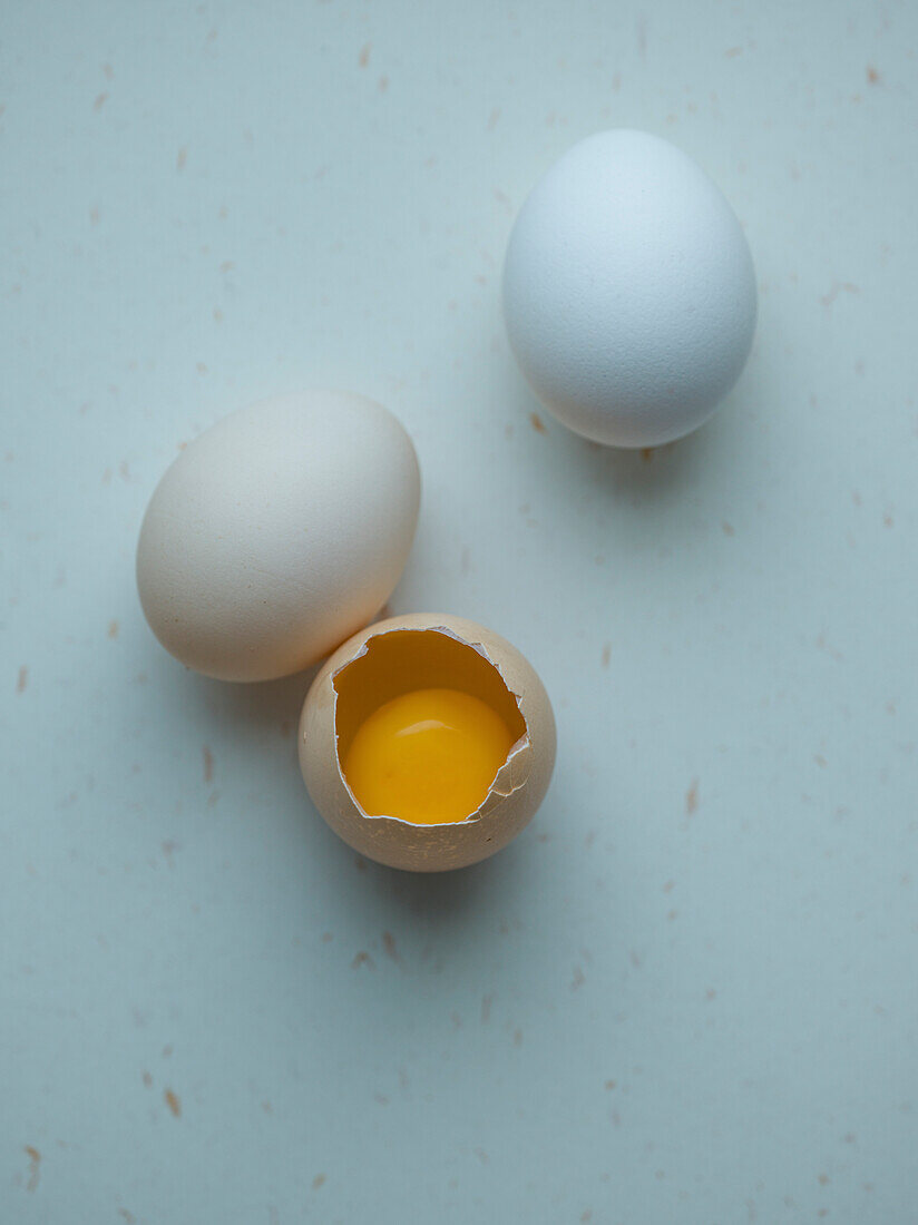 Three chicken eggs on a white background, one of them burst open