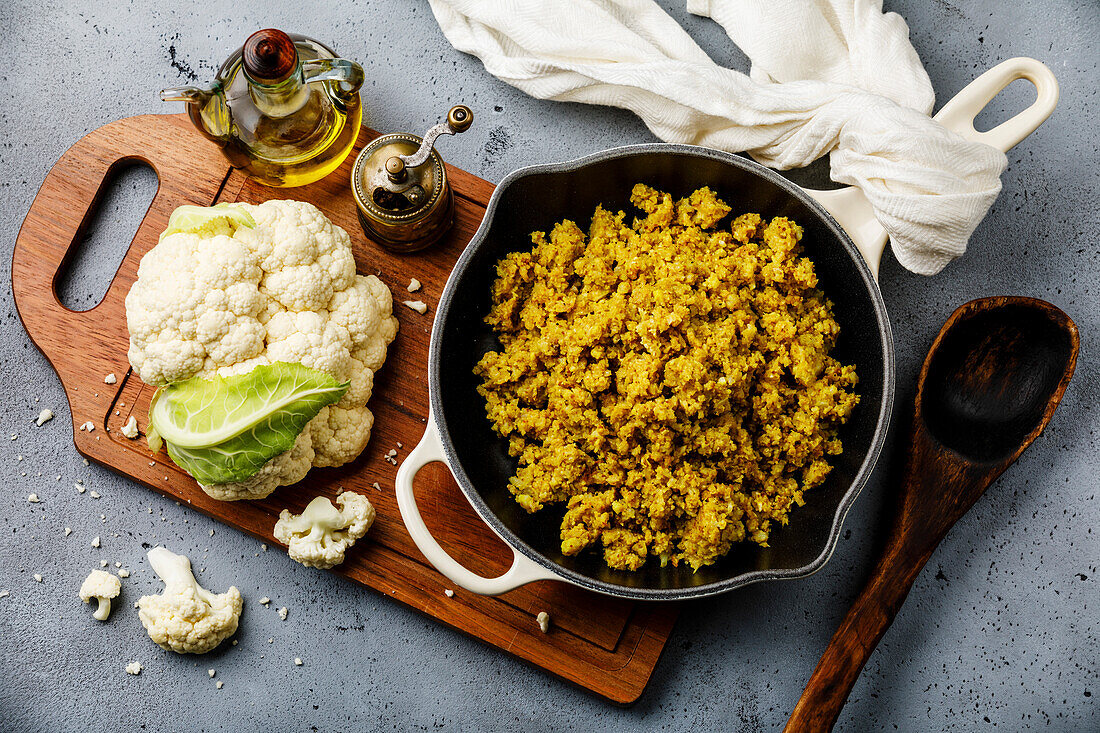 Cauliflower rice with spices in a pan and raw cauliflower on a concrete background