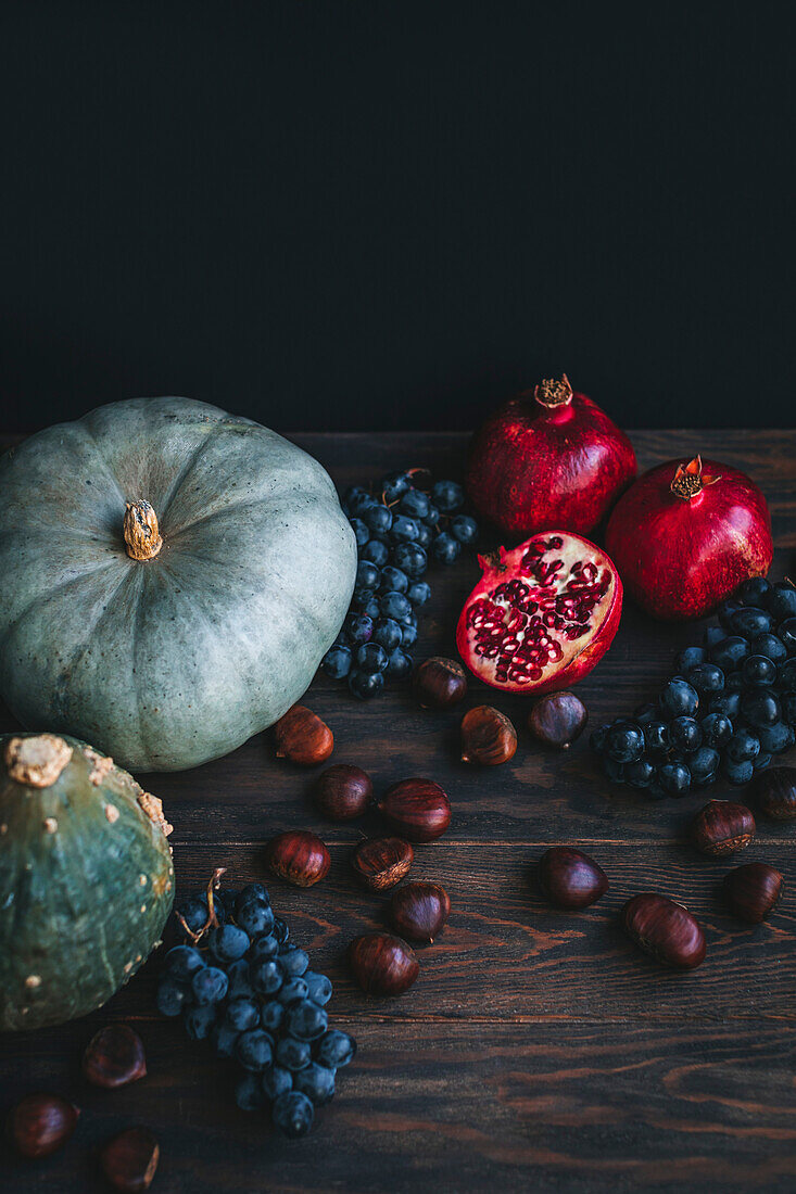 Herbstliche Produkte auf dunklem Hintergrund, darunter Kürbisse, Trauben, Kastanien und Granatäpfel
