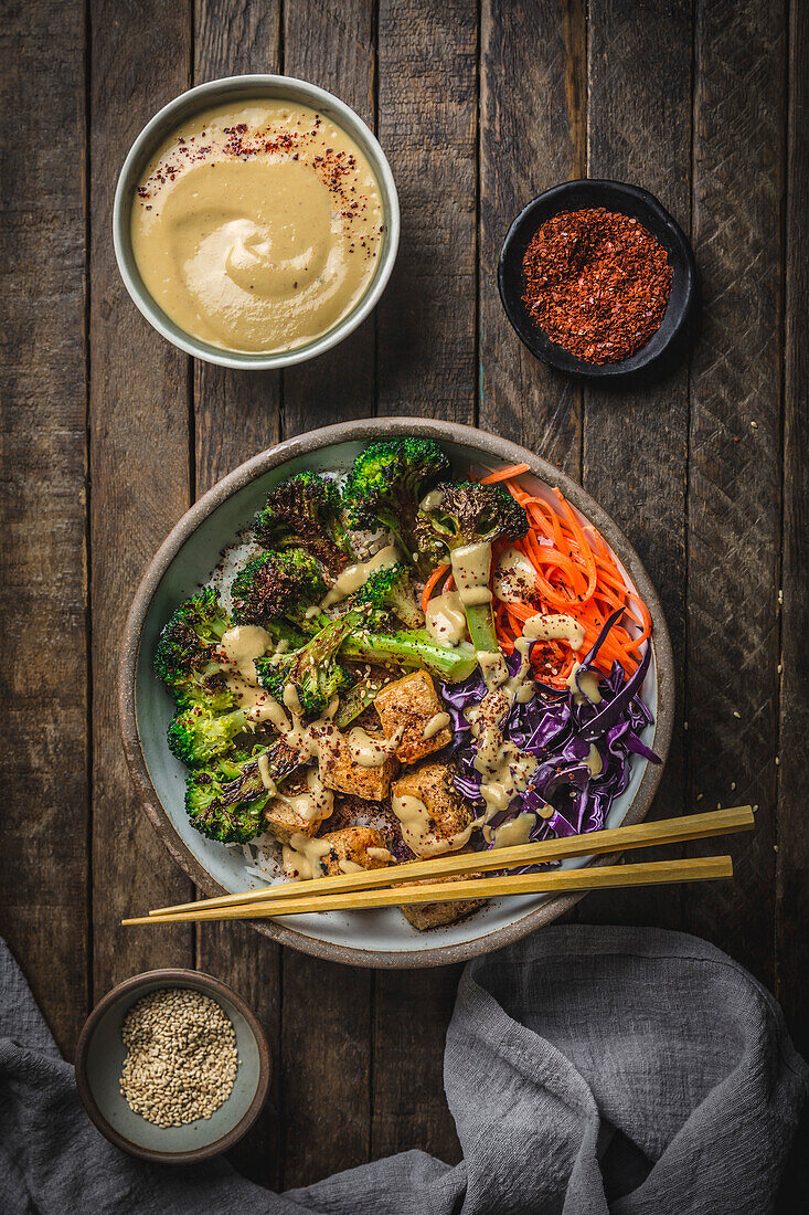 Charred Broccoli, Tofu, carrots and red cabbage Bowl with sauce and chopsticks