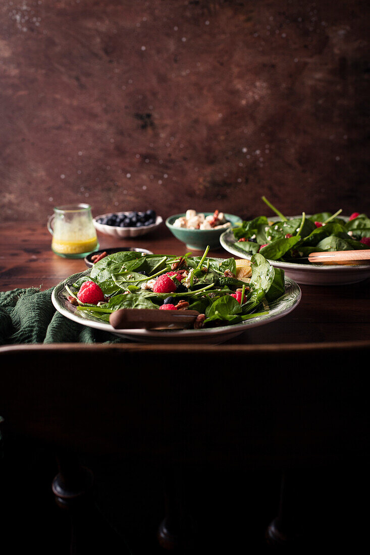 A healthy green salad with spinach, apple and raspberries in two bowls on a wooden table