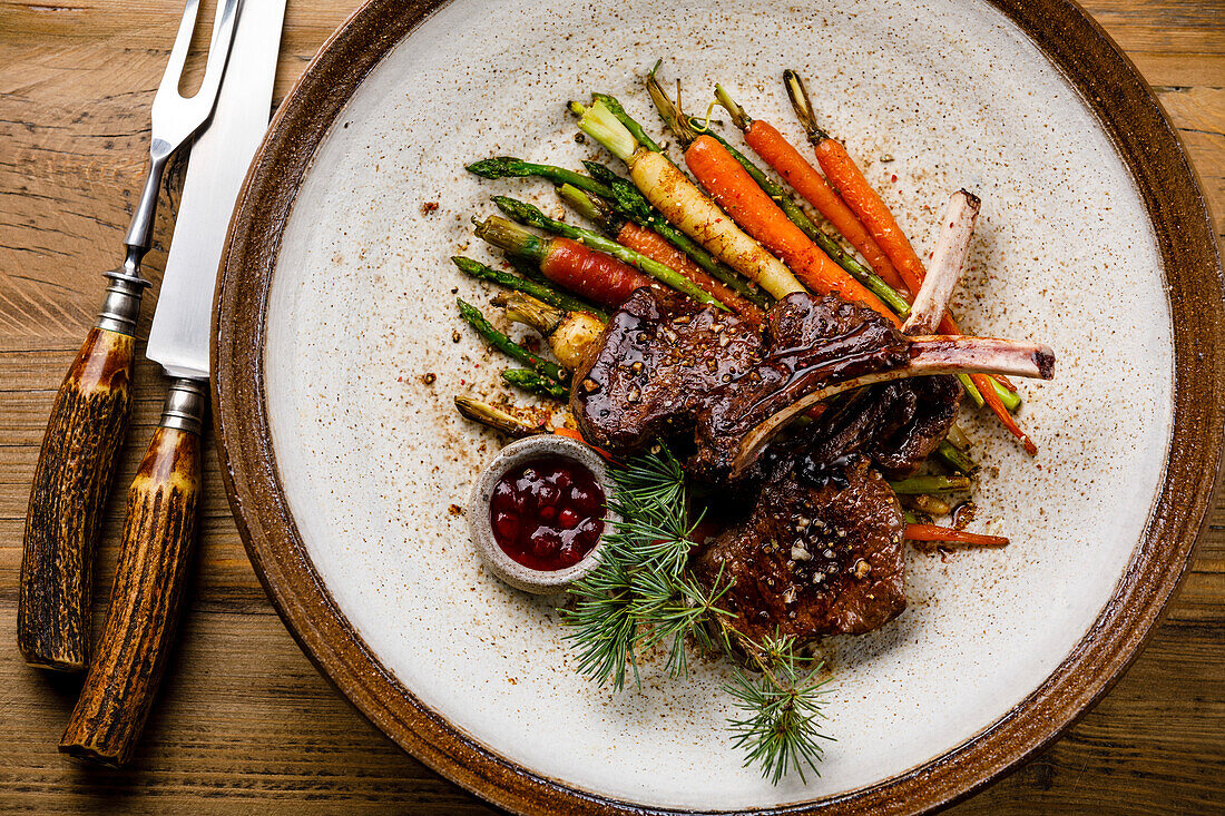 Grilled venison ribs with baked vegetables and berry sauce on a wooden base