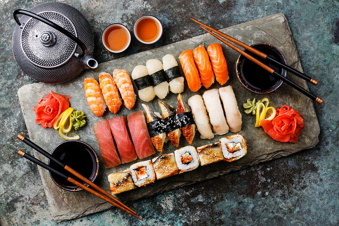 Sushi set, nigiri and sushi rolls with tea, served on a grey slate plate with metal background