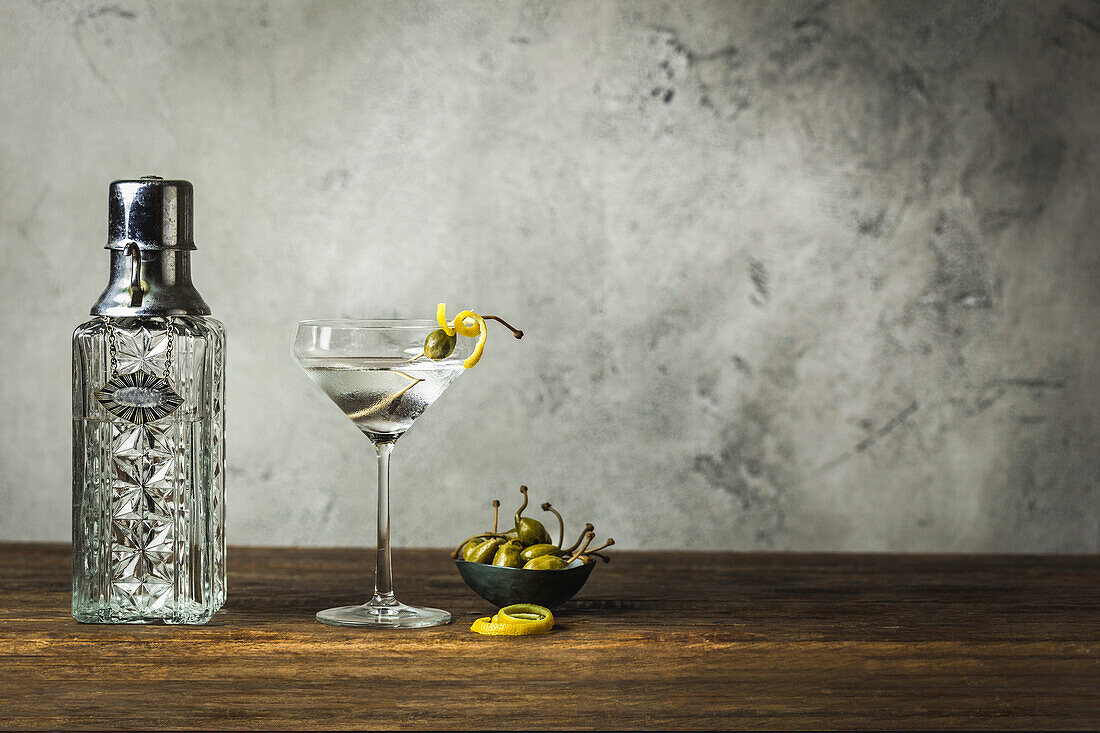Martini with lemon twist and caper berries, vintage decanter, caper berries in a small bowl