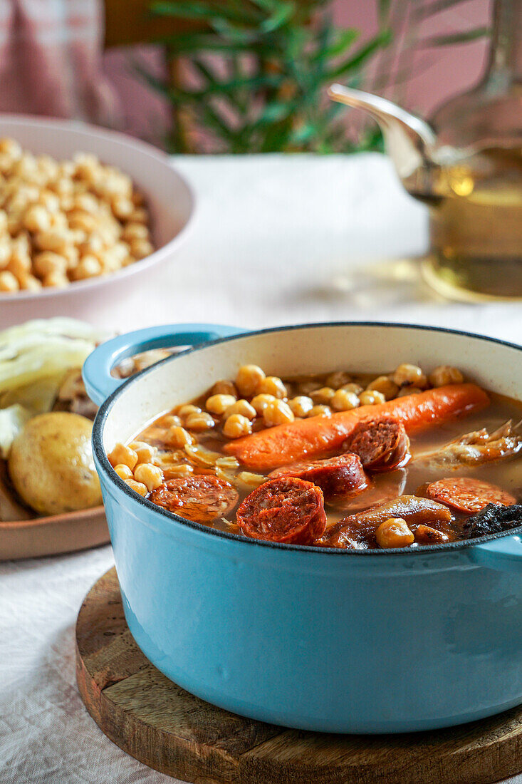 Cocido Madrileño, a traditional Spanish meal, chickpea-based stew from Madrid rose pink ceramic tile background