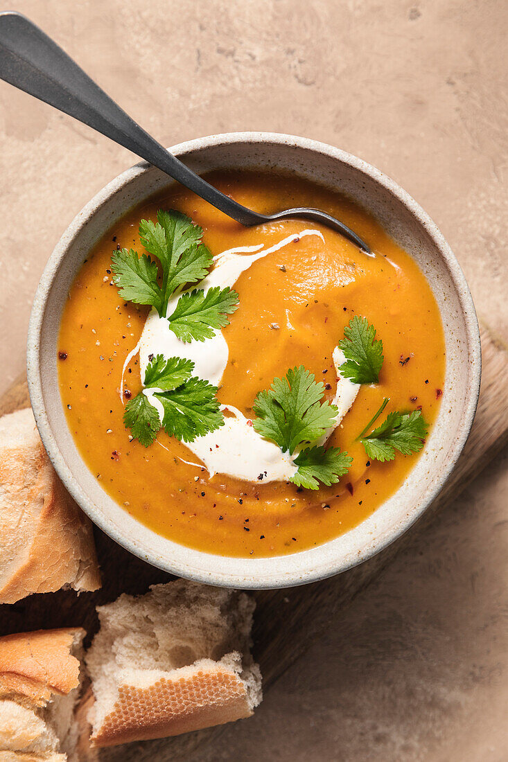 Butternusskürbissuppe und Baguette auf Holzbrett