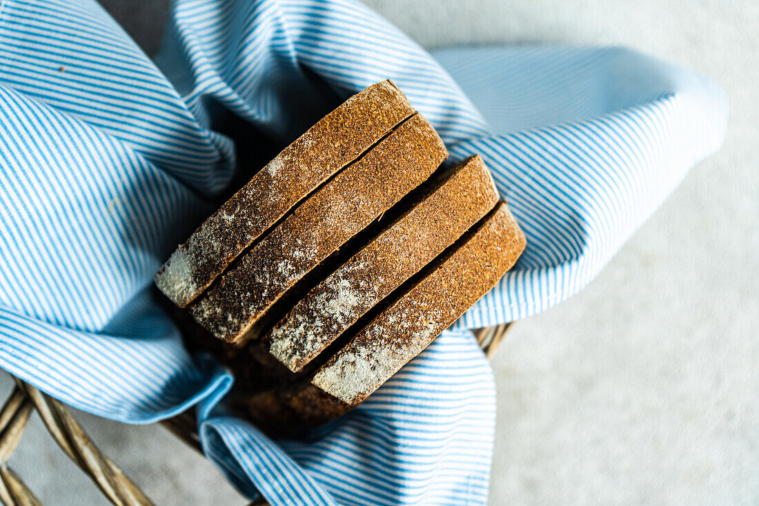 Top view of stack of rye bread slices in wicker basket with blue cloth napkin against blurred light background