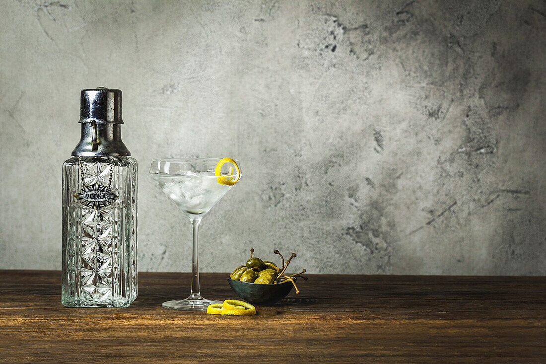 Martini on ice with lemon twist, vintage carafe, caper berries in small bowl