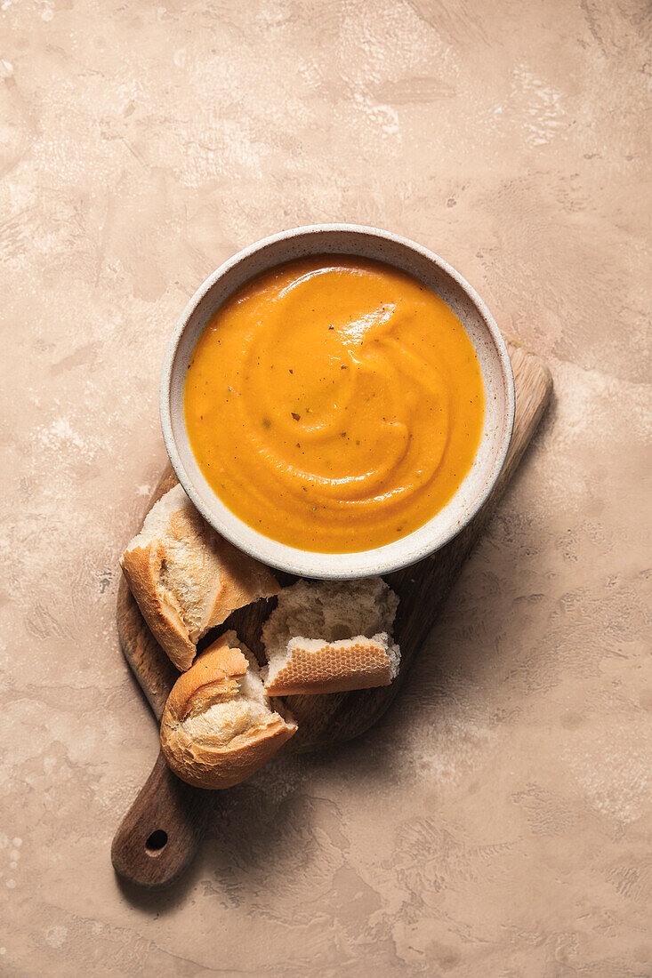 Butternusskürbissuppe und Baguette auf Holzbrett