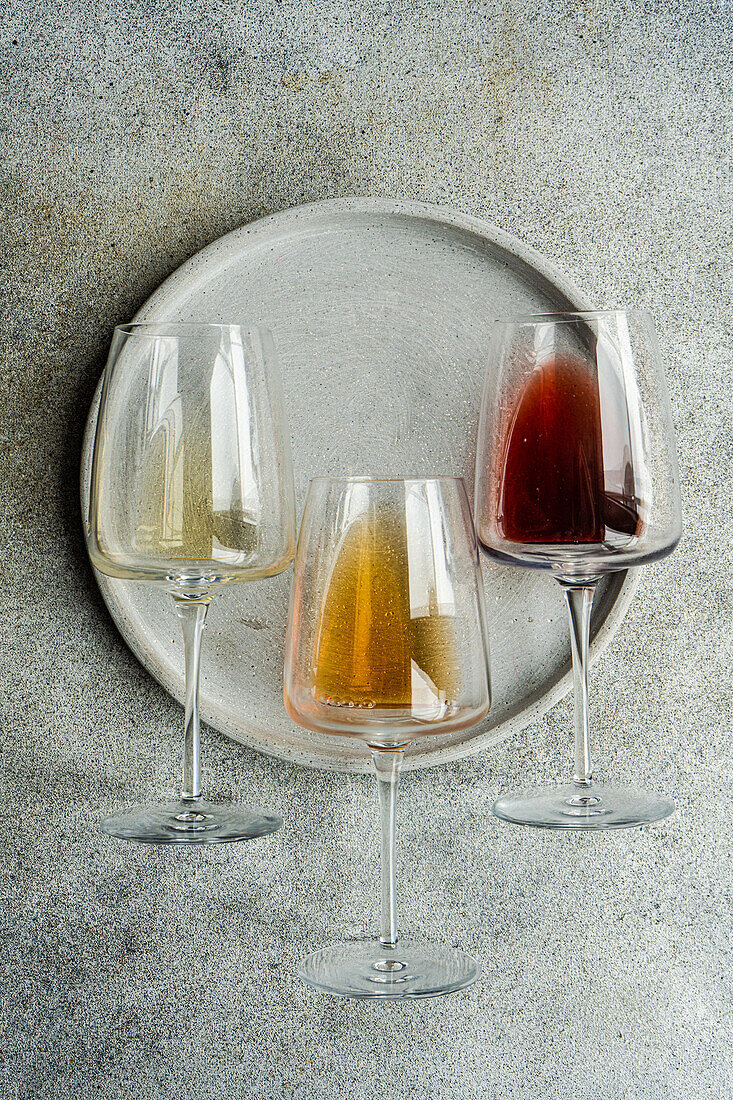 High angle of three varieties of Georgian dry wine glasses (white, amber and red) lying on a plate on concrete grey table