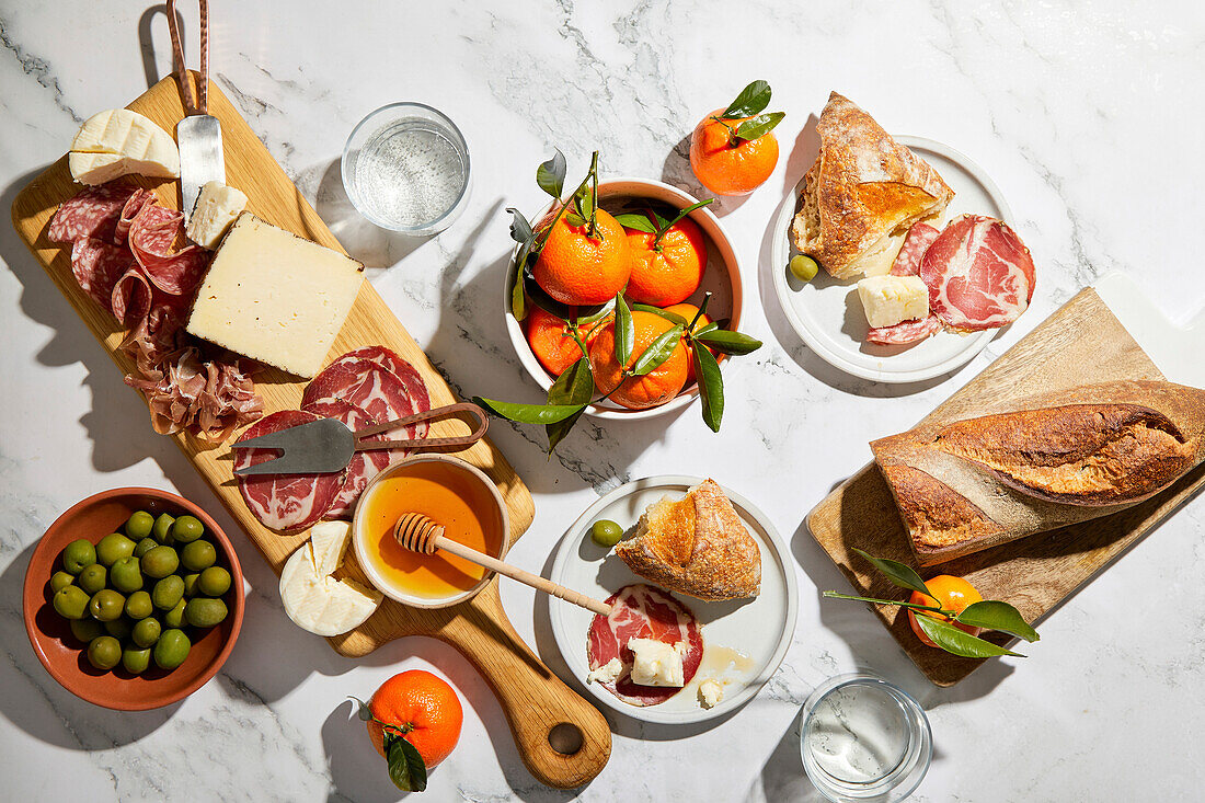 Charcuterie board with olives, charcuterie, cheese, bread and oranges on a marble background
