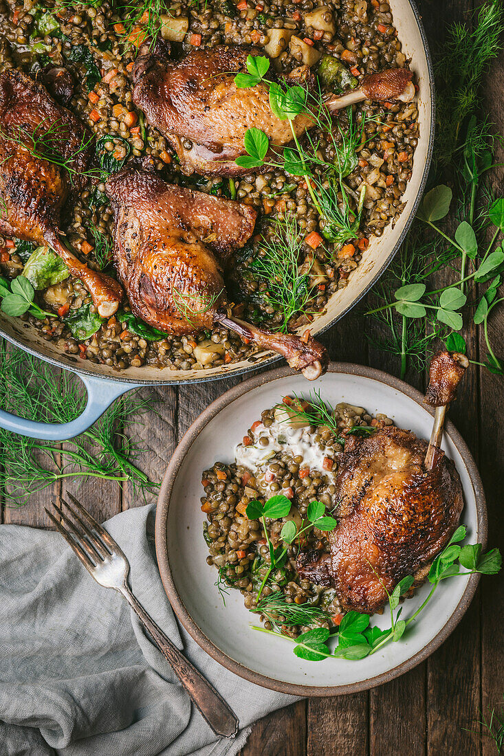 Duck legs on lentils in a casserole and a serving dish with pea shoots on the side