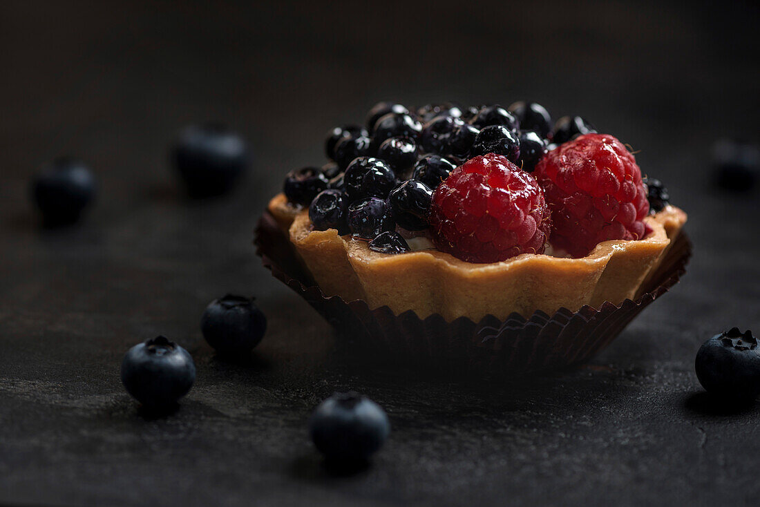 Pastry basket with blueberries and raspberries. Cake on a dark background