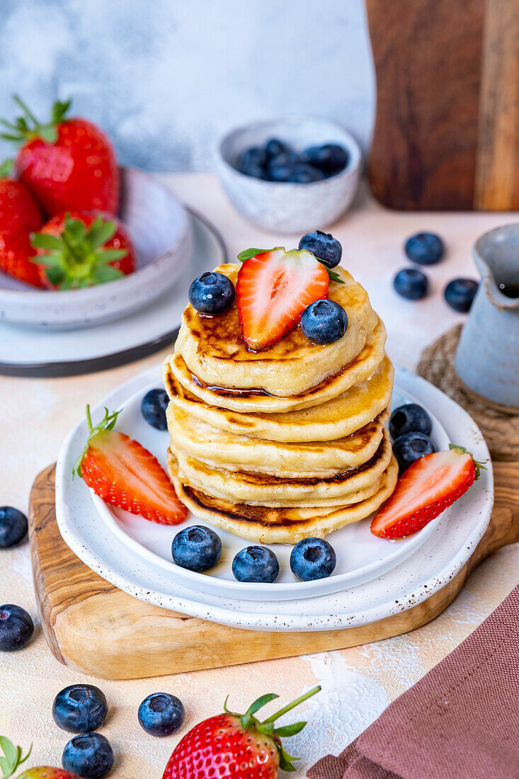 A stack of pancakes garnished with blueberries and strawberries on a white plate.