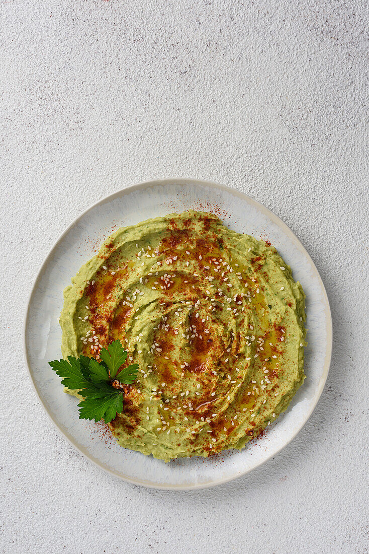 Avocado hummus flavoured with sesame, paprika and parsley. View from above
