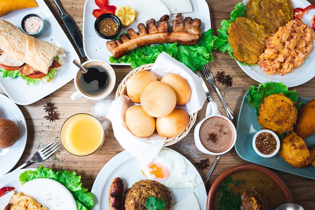Top view of an array of appetising Colombian dishes with papas rellenas pan de bono chicharron bunuelos and caldo de costilla with various drinks on a wooden table in a restaurant
