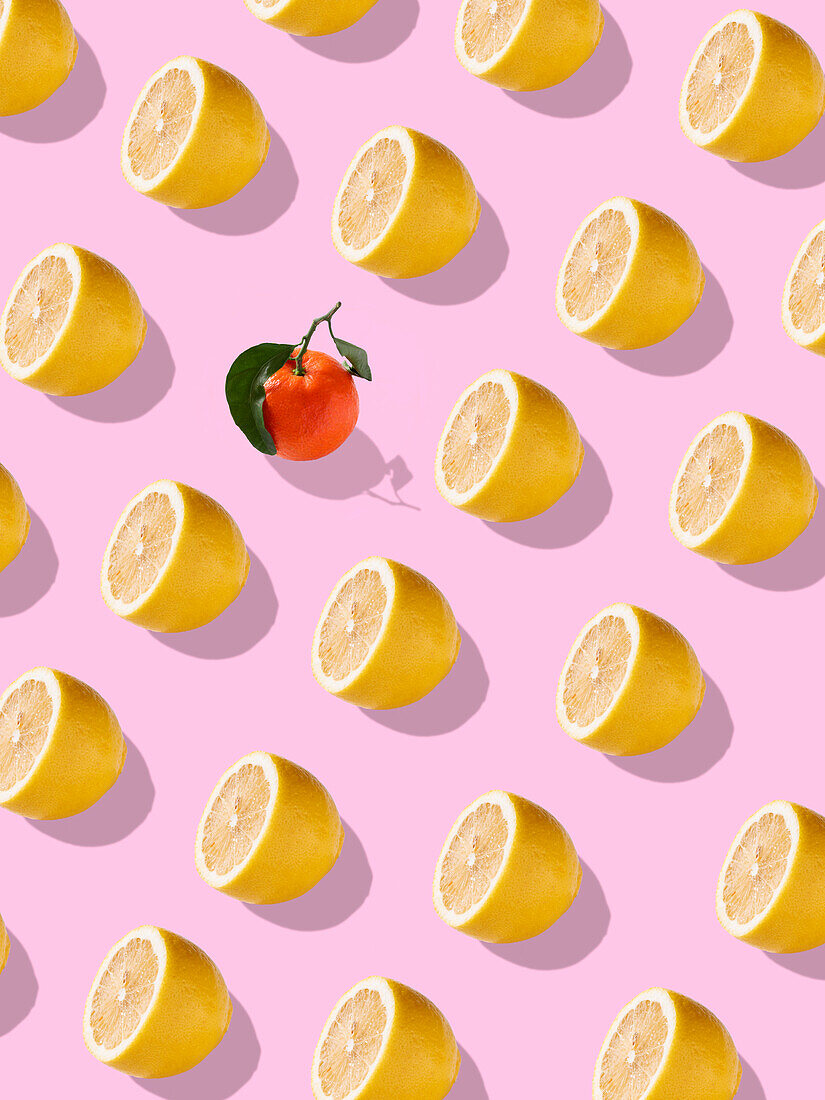 Full frame background of ripe juicy lemon halves and lonely orange with green leaves placed on bright pink backdrop