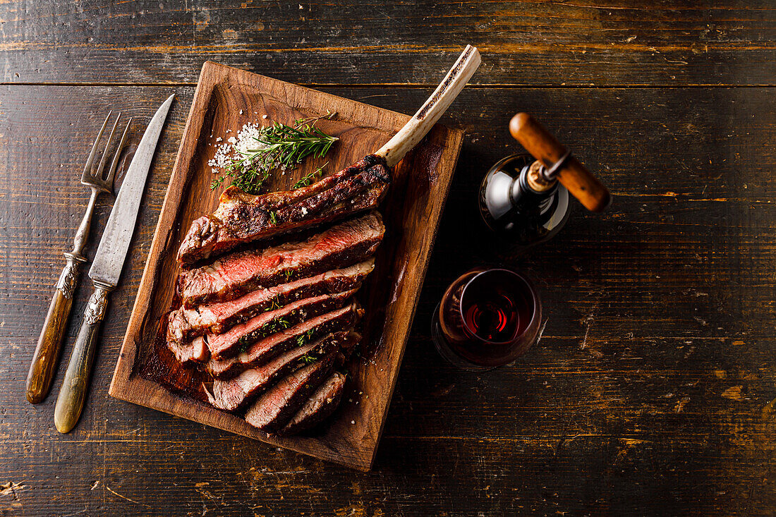Gegrilltes Tomahawk Steak am Knochen und ein Glas Rotwein auf Holzuntergrund