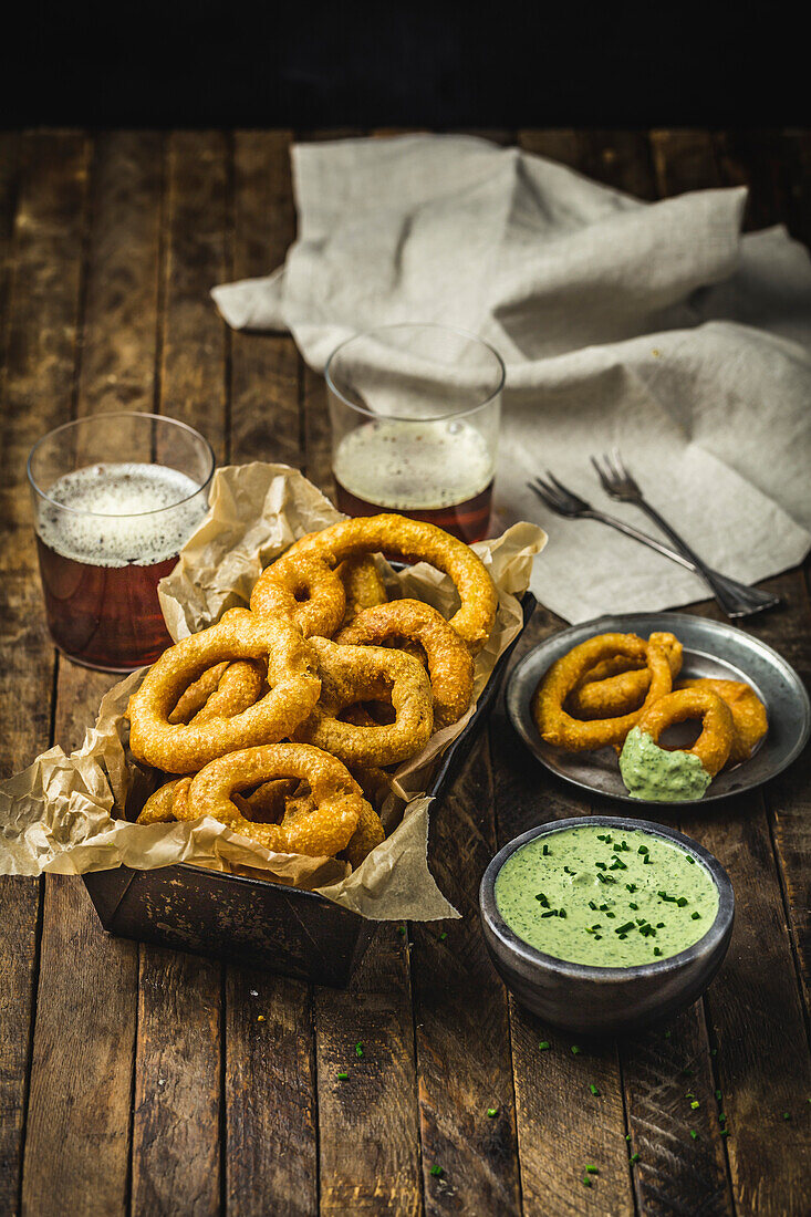 Baked onion rings on a metal basket with herb sauce and beer glasses
