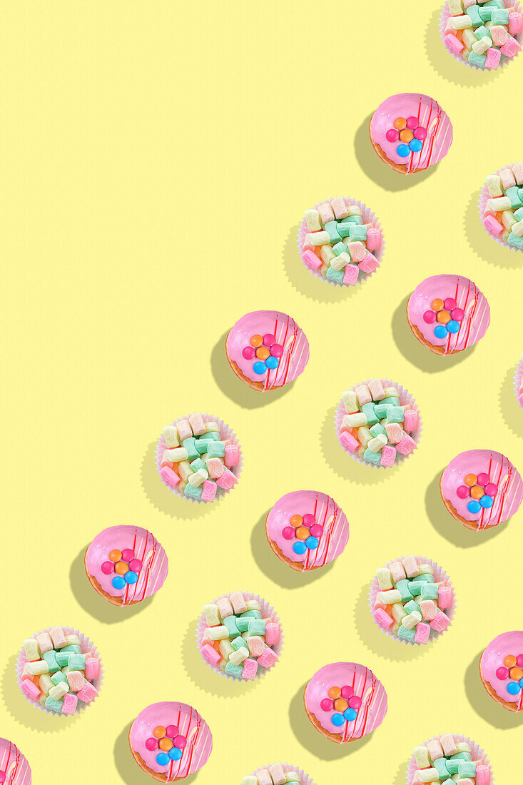 Modernes Retro-Farbmuster mit rosa Donuts und pastellfarbenen Bonbons auf gelbem Hintergrund, mit Leerzeichen