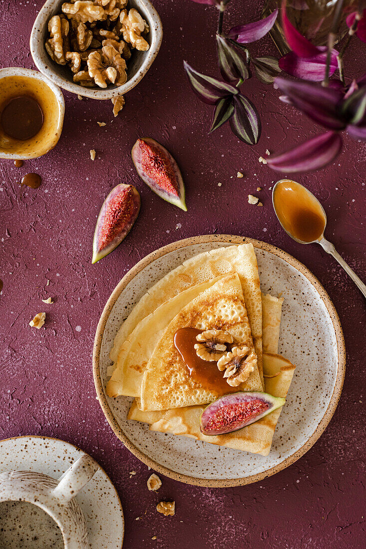 Crepes, folded on a handmade ceramic plate, decorated with figs, caramel and walnuts on a purple background