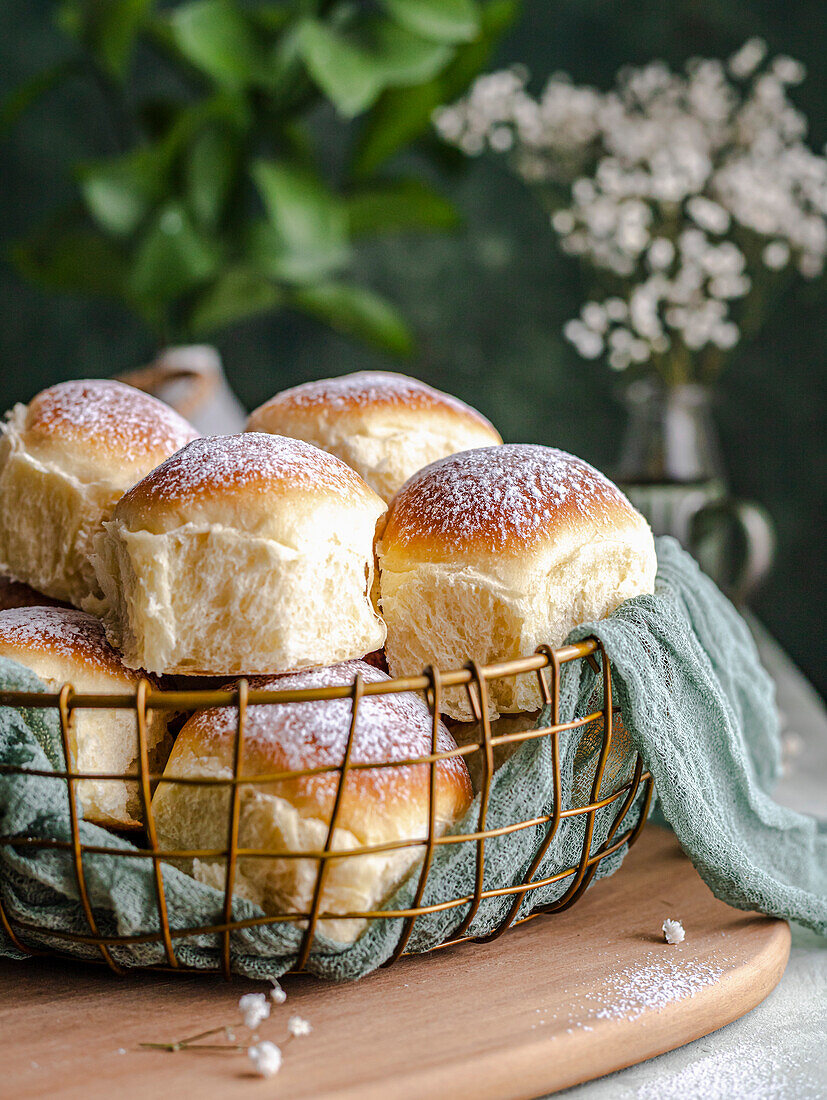 Homemade milk and cream cheese rolls in a basket with a cloth next to a window