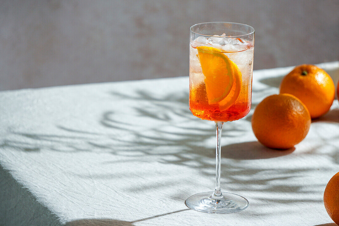 Aperol Spritz, Cocktail, auf einer Leinentischdecke, Schatten, hartes Sonnenlicht, Sommergetränk im Glas