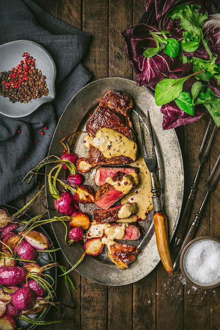 Sliced steak au poivre with cream sauce and roasted radishes on a metal plate