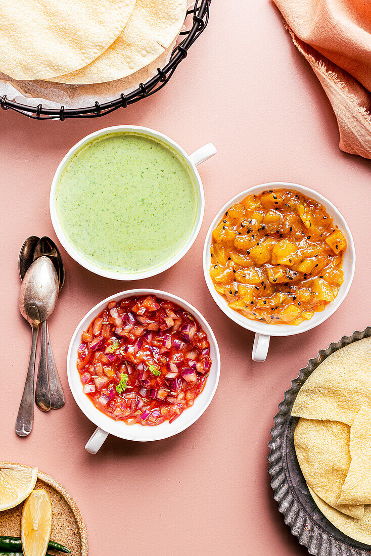 Three poppadom dips: mint yoghurt sauce, red onion chutney, mango chutney, served with poppadoms