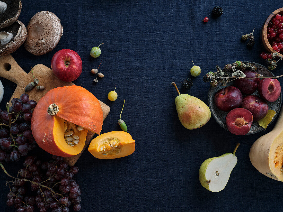 Autumnal food ingredients on a dark blue background with copy space. Flat-lay of autumn vegetables, berries and mushrooms from the local market. Vegan ingredients