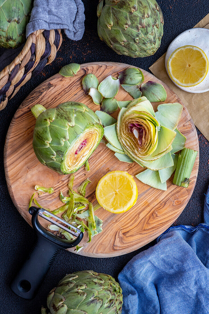 Sliced artichoke on a wooden board, with a slice of lemon and a peeler