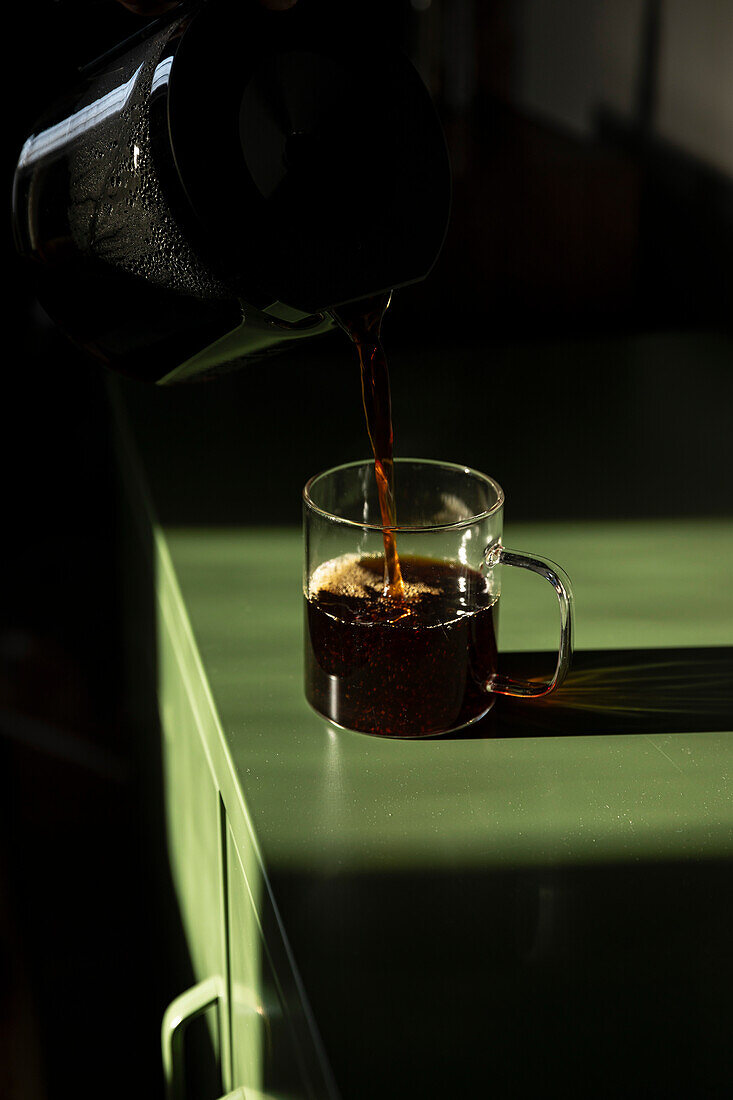 Coffee pouring into glass mug on green table.