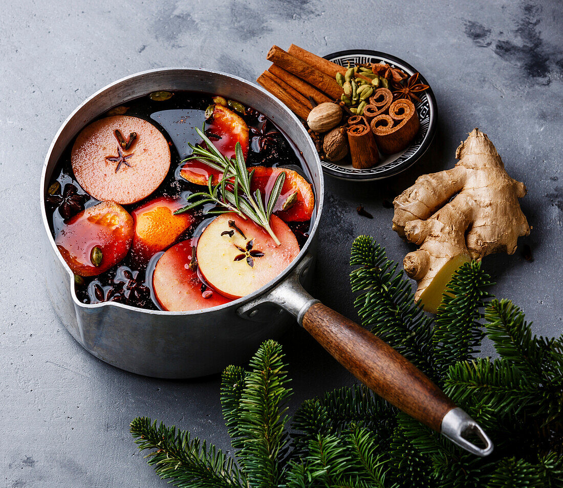 Mulled wine hot drink with citrus fruits, apples and spices in an aluminium casserole on a concrete backdrop