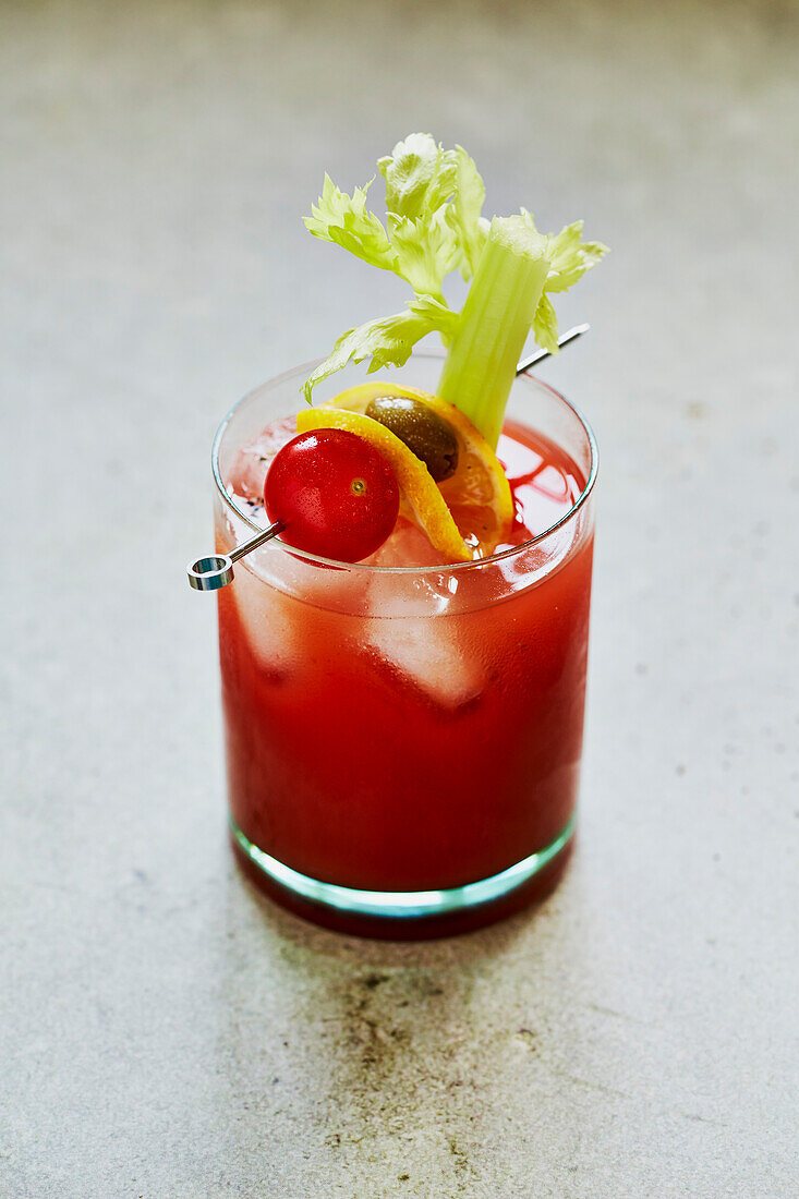 Bloody Mary Cocktail mit Sellerie-, Tomaten- und Olivengarnitur auf salbeigrünem Untergrund