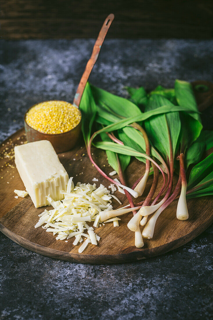 Wooden board with ingredients_wild ramps, cheddar cheese, polenta on dark background