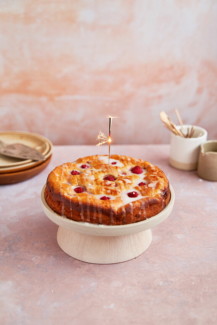 Raspberry and ricotta cake with icing on a stand and sparkler