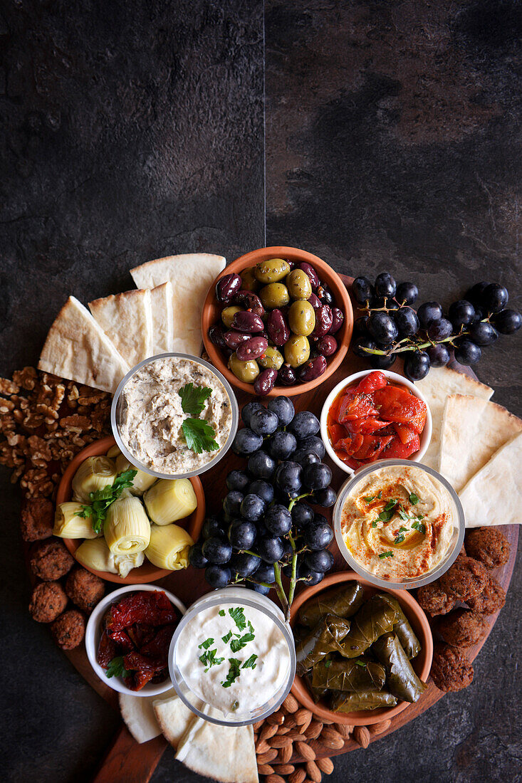 Mediterranean diet charcuterie board grazing platter on dark slate background, with negative copy space.