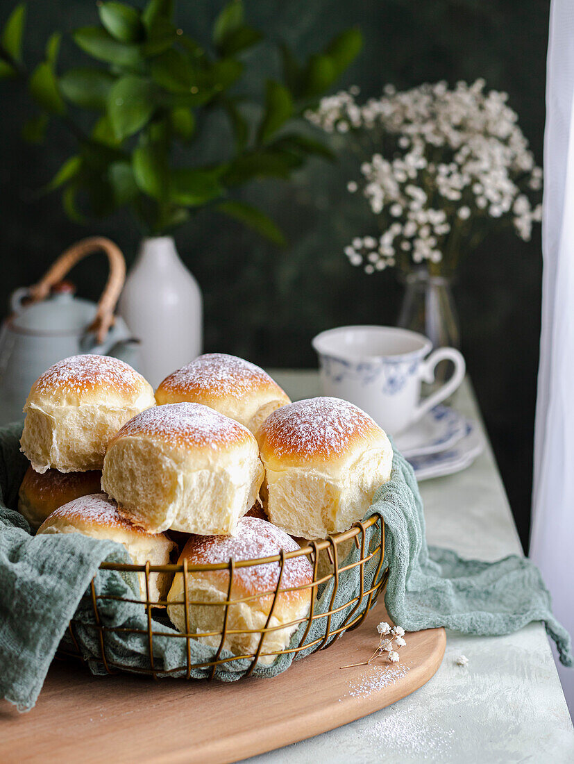 Homemade milk-cream-cheese rolls in a basket with a cloth next to a window