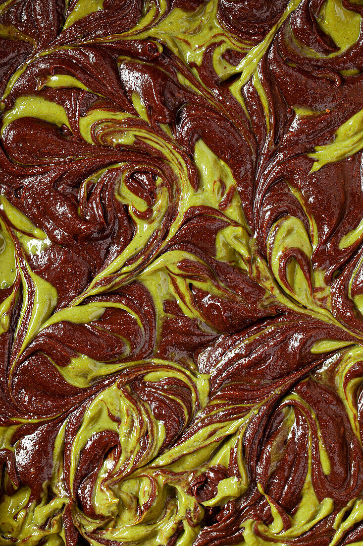 A close-up of brownies batter with a matcha cheesecake swirl through it.