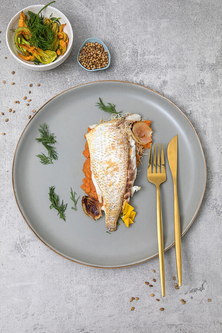 Freshly baked market fish served with fresh vegetables on a grey plate