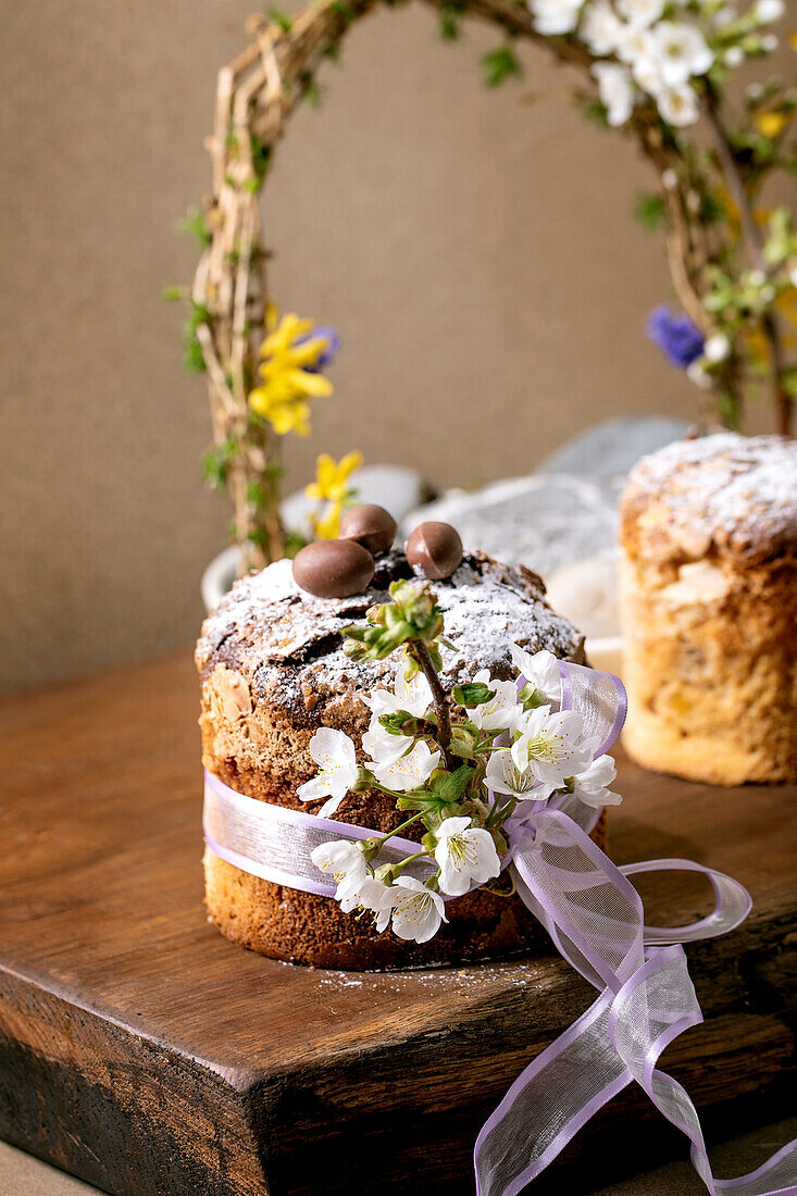 Homemade Italian traditional Easter panettone cake decorated with chocolate eggs, pink bow and blooming cherry tree flowers standing on wooden table. Traditional European Easter cake. Place to copy